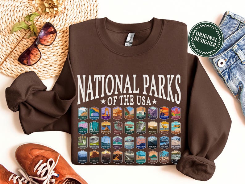 May include: Brown sweatshirt with the text "National Parks *of the USA*" in white. The sweatshirt features a grid of colorful patches representing different national parks.