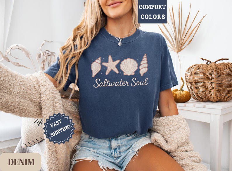 May include: A navy blue t-shirt with the words "Saltwater Soul" and seashell graphics. The shirt has a crew neck and short sleeves. The shirt is made of a soft, comfortable material.