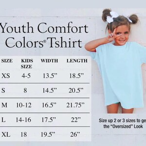 May include: A light blue t-shirt with a size chart titled Youth Comfort Colors Tshirt. The chart lists sizes XS through XL with corresponding kids' sizes, widths, and lengths in inches. Text at the bottom suggests sizing up for an oversized look.