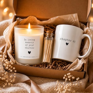 May include: A gift box containing a lit soy wax candle with a label reading In loving memory of your thirties, a small glass bottle filled with wooden matches, and a white ceramic mug with the text chapter 40 and a small heart icon.
