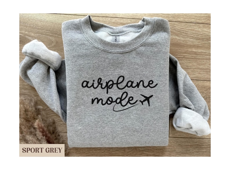 Puede incluir: Una sudadera gris con el texto "modo avi&oacute;n" y un peque&ntilde;o icono de avi&oacute;n impreso en la parte delantera.