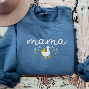May include: A blue sweatshirt with the word "mama" embroidered in white, along with a white embroidered duck and a yellow duckling.