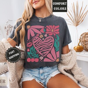May include: Dark gray t-shirt featuring a floral and heart design. The heart has a zebra print pattern. The shirt also has the text "Comfort Colors" printed on it.