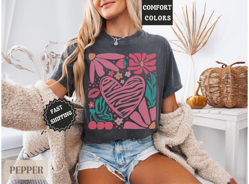 May include: Dark gray t-shirt featuring a floral and heart design. The heart has a zebra print pattern. The shirt also has the text "Comfort Colors" printed on it.