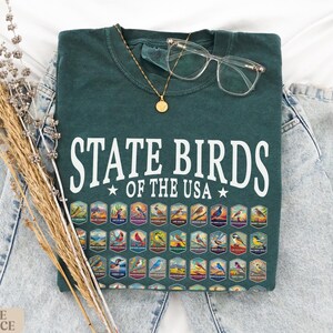 May include: A dark green t-shirt with the text "State Birds of the USA" in white. The shirt features a graphic of all 50 state birds in colorful illustrations.