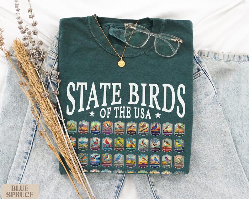 May include: A dark green t-shirt with the text "State Birds of the USA" in white. The shirt features a graphic of all 50 state birds in colorful illustrations.