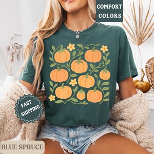 May include: Dark teal t-shirt featuring a pumpkin graphic. The design includes orange pumpkins, green vines, and yellow flowers. The words "COMFORT COLORS" are printed at the top right.