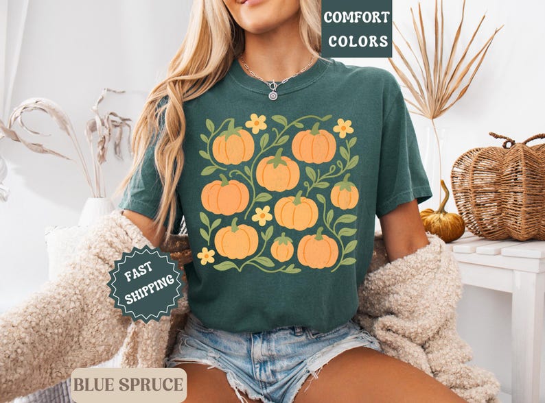 May include: Dark teal t-shirt featuring a pumpkin graphic. The design includes orange pumpkins, green vines, and yellow flowers. The words "COMFORT COLORS" are printed at the top right.