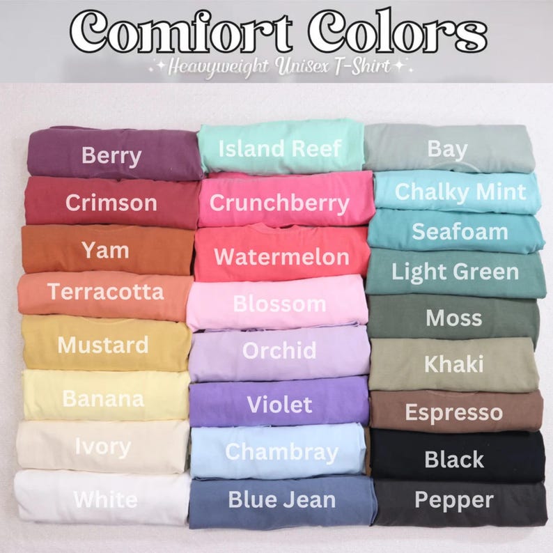 Op de afbeelding: Een display van gevouwen Comfort Colors unisex t-shirts in diverse kleuren. De afbeelding toont een reeks tinten, waaronder Berry, Crimson en Mustard, waarbij elk shirt is gelabeld met zijn kleurnaam. De tekst "Comfort Colors" staat bovenaan.
