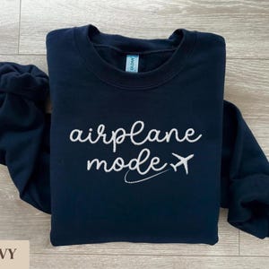 Puede incluir: Una sudadera azul marino con el texto "airplane mode" bordado en blanco y un peque&ntilde;o avi&oacute;n gr&aacute;fico.