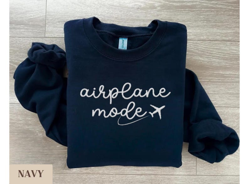 Puede incluir: Una sudadera azul marino con el texto "airplane mode" bordado en blanco y un peque&ntilde;o avi&oacute;n gr&aacute;fico.