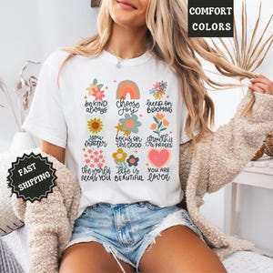 Pu&ograve; includere: Maglietta bianca con un design floreale colorato e affermazioni positive, tra cui "sii sempre gentile", "scegli la gioia", "continua a fiorire", "tu conti", "concentrati sul bene", "la crescita &egrave; un processo", "il mondo ha bisogno di te", "la vita &egrave; bella" e "sei amato".