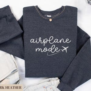 Puede incluir: Sudadera gris oscuro jaspeada con el texto "modo avi&oacute;n" y un avi&oacute;n blanco.