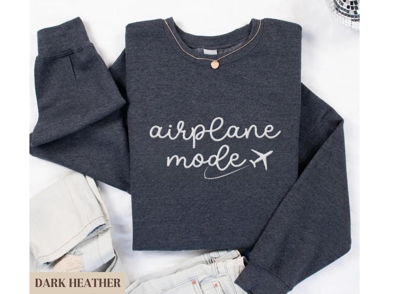 Puede incluir: Sudadera gris oscuro jaspeada con el texto "modo avi&oacute;n" y un avi&oacute;n blanco.