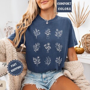 May include: A navy blue t-shirt with a white floral design. The shirt has the text "Comfort Colors" printed on the top left corner.