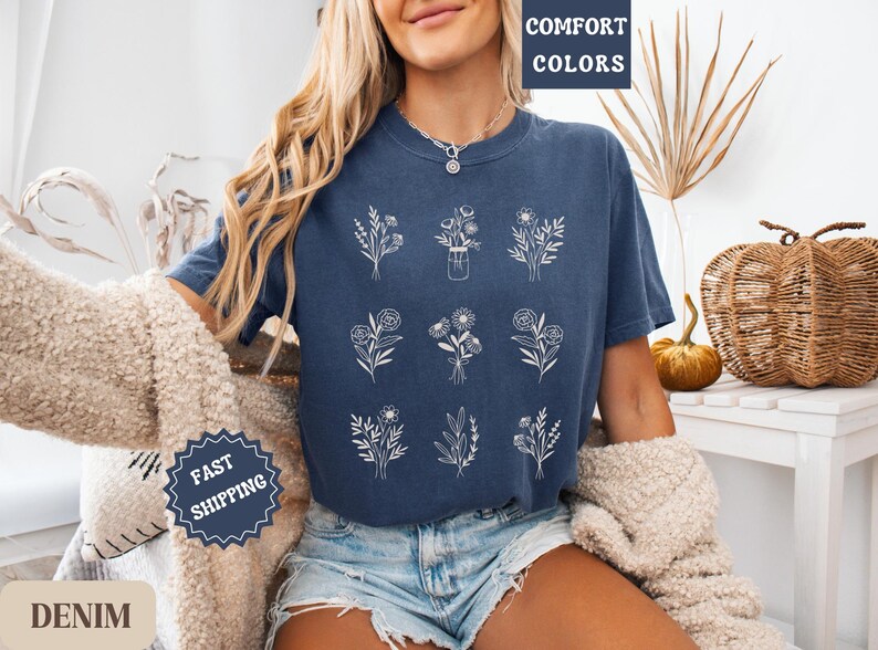 May include: A navy blue t-shirt with a white floral design. The shirt has the text "Comfort Colors" printed on the top left corner.