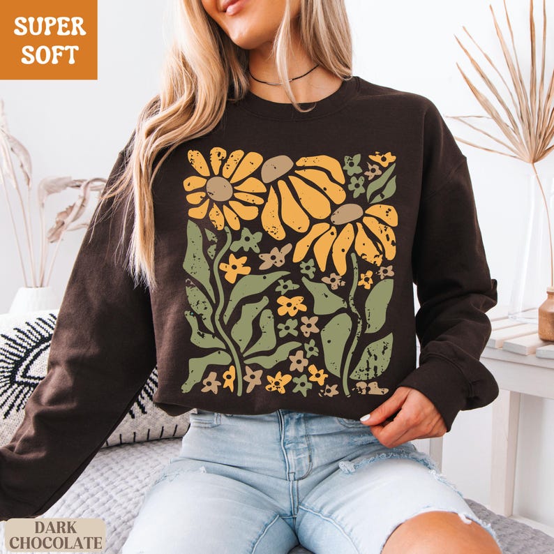 May include: Dark chocolate-colored sweatshirt with a floral design. The graphic features large yellow flowers, green leaves, and smaller flowers. The words "SUPER SOFT" and "DARK CHOCOLATE" are printed on the image.