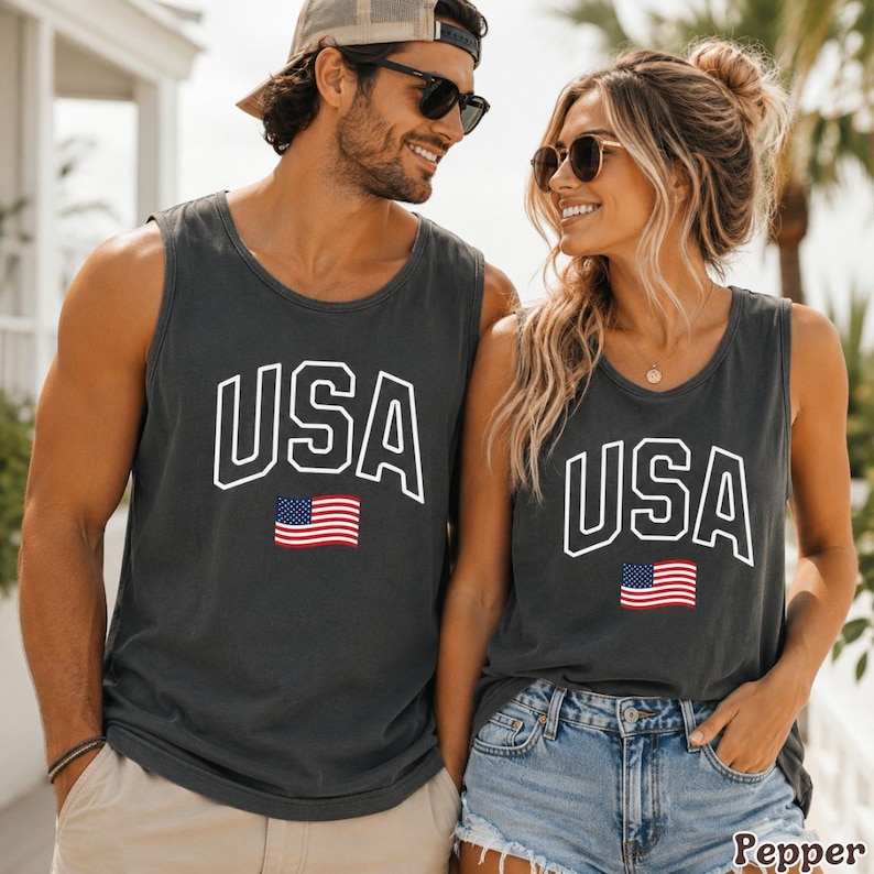Peut inclure: Deux personnes portant des d&eacute;bardeurs gris anthracite assortis. Chaque d&eacute;bardeur porte le mot "USA" en lettres blanches avec un contour blanc et un petit drapeau am&eacute;ricain en dessous. Les d&eacute;bardeurs sont sans manches.