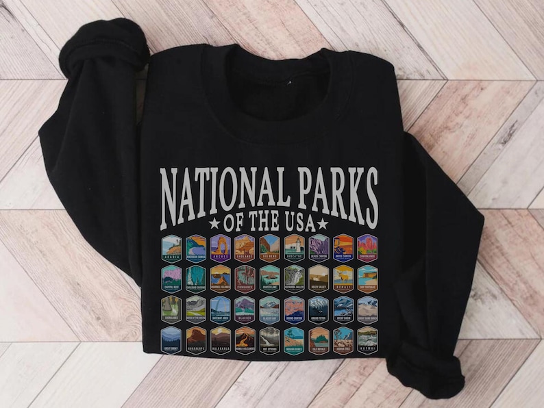 May include: Black t-shirt with the text "National Parks of the USA" in white lettering. The shirt features a grid of colorful national park logos.
