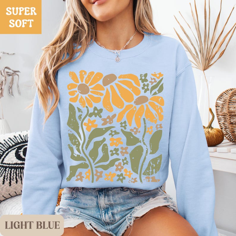 May include: Light blue sweatshirt with a floral design in shades of yellow, brown, and green. The sweatshirt has the words "SUPER SOFT" in a yellow box. The words "LIGHT BLUE" are at the bottom of the image.