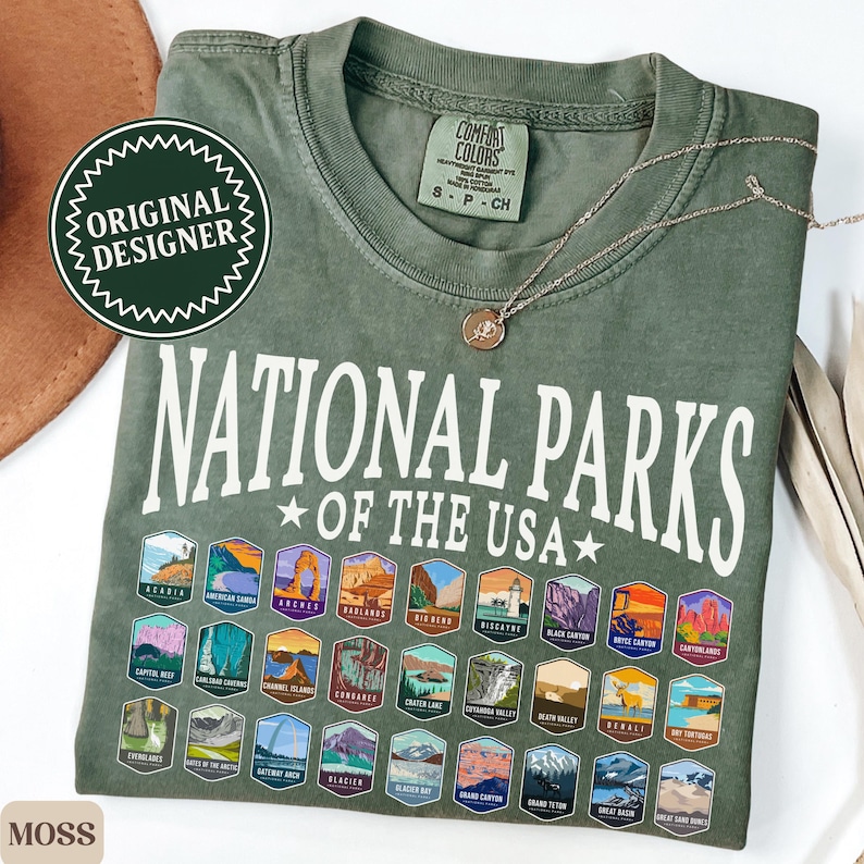 以下が含まれることがあります： アメリカの国立公園のロゴがすべて描かれた、緑色のTシャツ。Tシャツには「National Parks of the USA」の文字が書かれています。