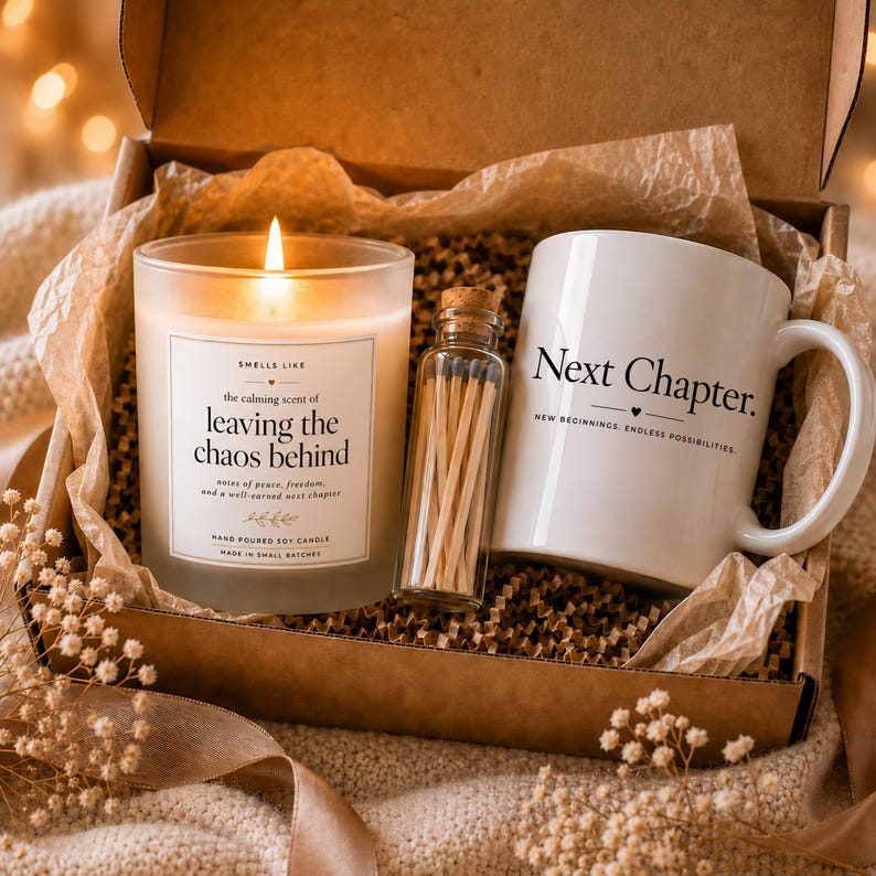 May include: A gift box containing a lit soy candle in a glass jar with a label reading 'Smells like the calming scent of leaving the chaos behind', a small glass bottle filled with wooden matches, and a white ceramic mug printed with 'Next Chapter'.