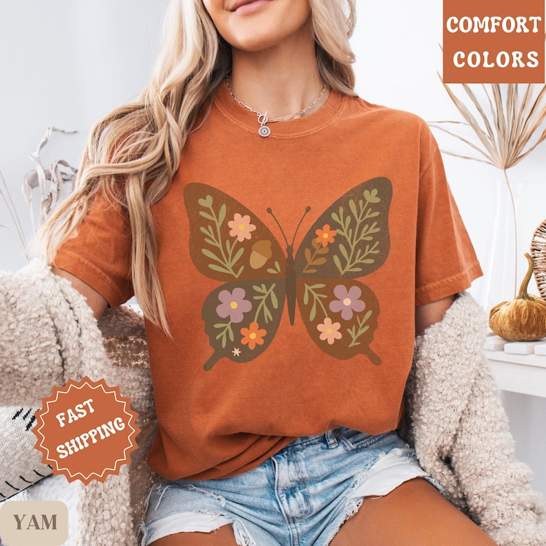 Peut inclure: T-shirt orange br&ucirc;l&eacute; avec un motif de papillon orn&eacute; de motifs floraux et de feuilles marron, roses et oranges. Le t-shirt porte les mots "COMFORT COLORS" et "FAST SHIPPING".