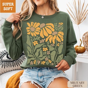 May include: Olive green sweatshirt with a floral design featuring large yellow and brown sunflowers and smaller flowers. The words "SUPER SOFT" are in a brown box in the upper left corner. The words "MILITARY GREEN" are in a brown box in the lower right corner.