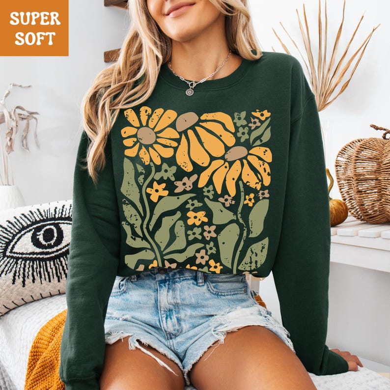 May include: Dark green sweatshirt with a floral design. The graphic features large yellow and brown flowers, smaller yellow flowers, and green leaves. The words "SUPER SOFT" are in an orange box in the upper left corner.