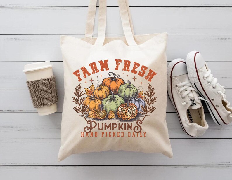 May include: A white canvas tote bag with the text "Farm Fresh Pumpkins Hand Picked Daily" in orange and brown. The bag features a vintage illustration of pumpkins in various colors and sizes.