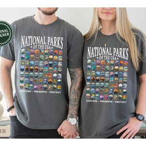 以下が含まれることがあります： アメリカの国立公園のすべてが描かれたグレーのTシャツが2枚。シャツには「National Parks of the USA」と「Explore - Preserve - Protect」の文字が書かれています。