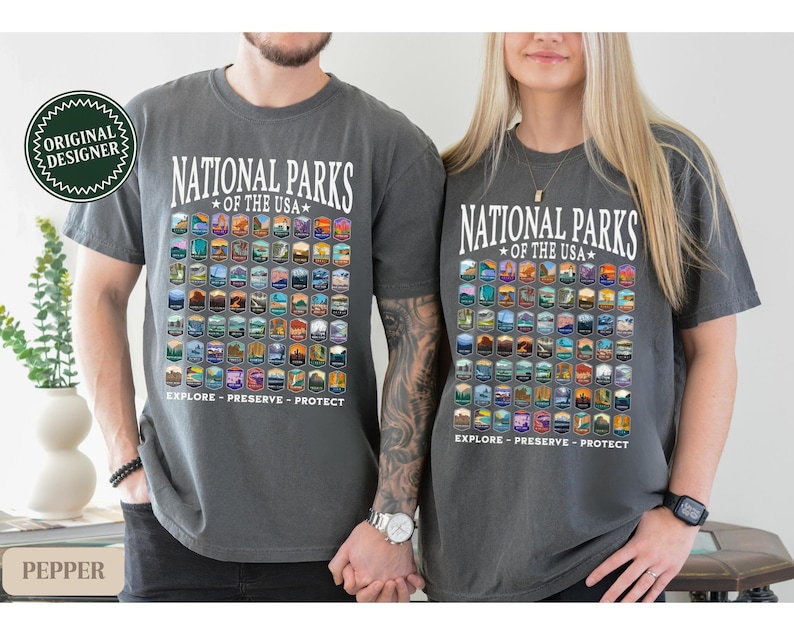 以下が含まれることがあります： アメリカの国立公園のすべてが描かれたグレーのTシャツが2枚。シャツには「National Parks of the USA」と「Explore - Preserve - Protect」の文字が書かれています。