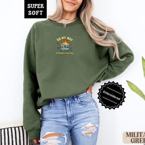 Pu&ograve; includere: Felpa verde militare con grafica ricamata. Il design presenta un'immagine a cartoni animati con il testo "ON MY WAY To Brighten Your Day". La felpa &egrave; etichettata "SUPER SOFT" e "Embroidered".