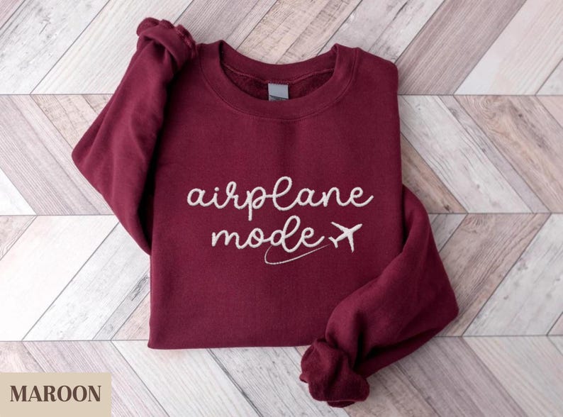 Puede incluir: Una sudadera color burdeos con el texto "airplane mode" y un avi&oacute;n blanco.