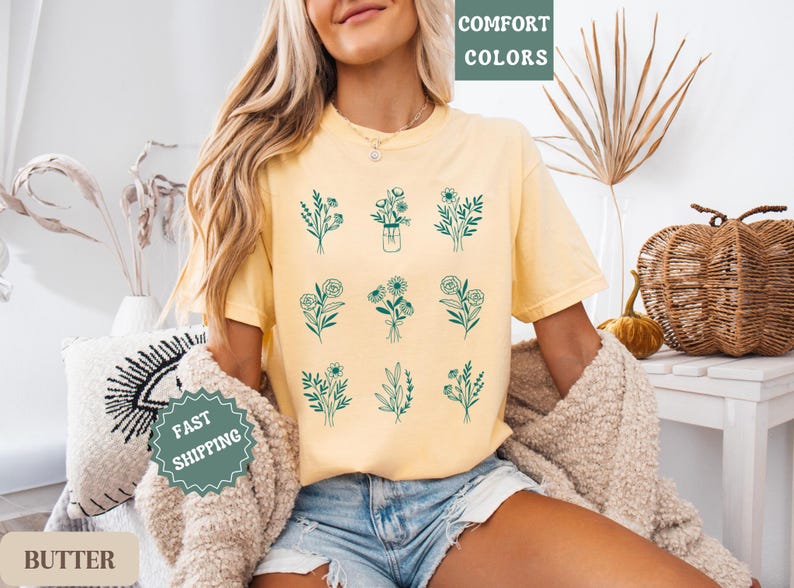 May include: A yellow t-shirt with a floral design. The shirt has a crew neck and short sleeves. The design features nine different floral arrangements in a green color. The text "COMFORT COLORS" is printed on the top of the shirt.