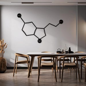 May include: A black metal wall sculpture depicting the chemical structure of serotonin, a neurotransmitter associated with mood and happiness. The sculpture is mounted on a white wall above a wooden dining table with six chairs.