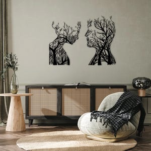 May include: Two black metal wall art pieces showing human profiles with tree-like patterns. The artwork is mounted on a light-coloured wall above a dark wood cabinet. The room has a modern, minimalist aesthetic.
