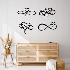May include: Four black metal wall art pieces featuring infinity symbols with heart designs. The art is mounted on a white wall above a wooden dresser. The designs vary, with some featuring intertwined hearts and others a single heart.