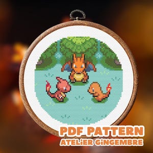 May include: A cross-stitch embroidery of three cartoon characters in a water scene, framed in a wooden hoop. The characters are orange, pink, and orange-yellow. The text "PDF PATTERN ATELIER GINGEMBRE" is at the bottom.