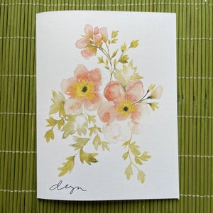 May include: A watercolor painting of a bouquet of pink and yellow flowers with green leaves. The flowers are painted in a loose, impressionistic style. The painting is signed "dezn" in the bottom left corner.