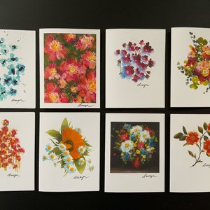 May include: Set of eight blank greeting cards featuring watercolor floral designs. Each card has a different floral pattern, including blue, red, orange, and purple flowers. The cards are all white with black lettering that says "design".