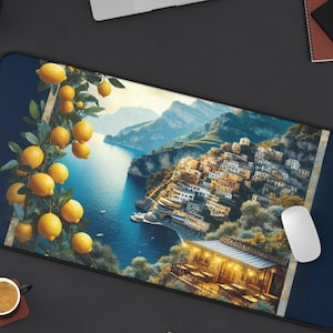 May include: A rectangular mouse mat with a coastal Italian village scene and a lemon tree. The design includes a blue sea, mountains, and a restaurant. The mat has a dark blue border and a white mouse.