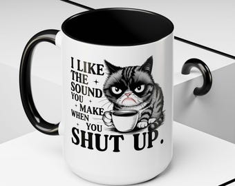 Peut inclure: Mug en céramique blanche avec intérieur, anse et bord noirs. La tasse présente une illustration de chat grincheux tenant une tasse à café, avec le texte "I LIKE THE SOUND YOU MAKE WHEN YOU SHUT UP."
