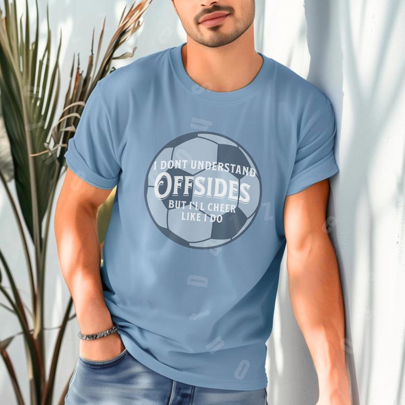 May include: Light blue t-shirt with the text "I DON'T UNDERSTAND OFFSIDES BUT I'LL CHEER LIKE I DO" in white and gray, with a soccer ball graphic. The shirt is a crew neck and has short sleeves.