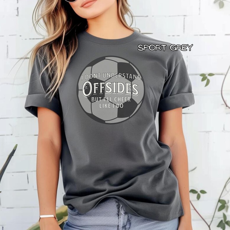 May include: Sport grey t-shirt with a soccer ball graphic. The graphic includes the text "I don't understand offsides but I'll cheer like I do". The shirt has short sleeves and a crew neck.