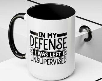 Peut inclure: Une tasse à café en céramique blanche avec une poignée noire et un bord noir. La tasse porte une inscription amusante imprimée en noir : "In my defense I was left unsupervised".