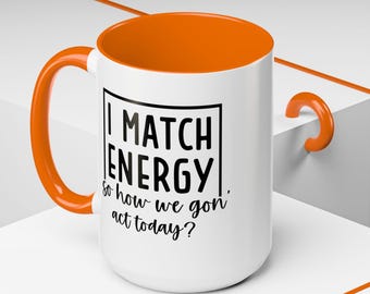Peut inclure: Une tasse en céramique blanche avec un bord et une poignée orange. La tasse a un texte noir qui dit "I MATCH ENERGY, so how we gon' act today?"