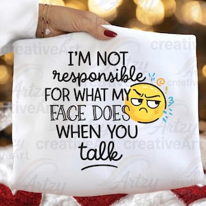 Könnte beinhalten: Weißes Kissen mit dem Text "I'M NOT responsible FOR WHAT MY FACE DOES WHEN YOU talk" in Schwarz. Ein gelbes, wütendes Emoji befindet sich auf der rechten Seite des Textes. Das Kissen wird von einer Person mit rotem Nagellack gehalten.