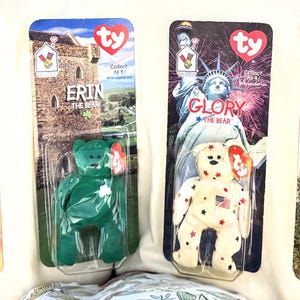 May include: Four Ty Beanie Baby collectible plush toys in their original packaging. The bears are named Britannia, Erin, Glory, and Maple. Each bear is in a clear plastic case with a themed background and a Ty heart tag.