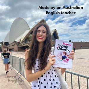 May include: A woman in a white and black polka dot dress holds a book titled "Beginner English Listening" with the text "Learn English A1" on the cover. The book is in front of the Sydney Opera House.